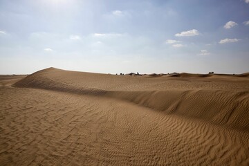 Scenic view of large desert landscape with sand dunes under blue cloudy sky