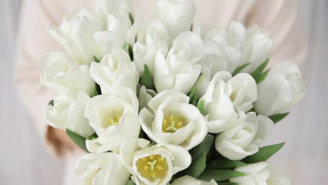 Close-up of large beautiful bouquet of delicate white tulips in the woman's hands. Bouquet of the first spring flowers. Concept for floristic business or flower delivery. shallow dof