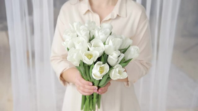 Unrecognizable caucasian woman holding large bunch of delicate white tulips, close up. Bouquet of the first spring flowers in the hands. Concept for floristic business or flower delivery. Shallow dof