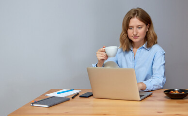 Beautiful young woman working on laptop while sitting at the living room, drinking coffee.