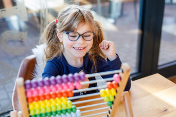 Little preschool girl playing with educational wooden rainbow toy counter abacus. Healthy happy...