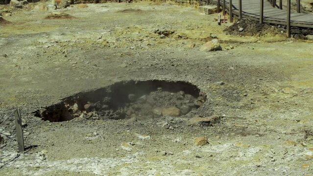Volcanic pit hole in the ground where mud is boiling. Steaming vents.