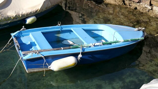 Old dilapidated plastic blue rowboat moored or anchored to rocky shoreline