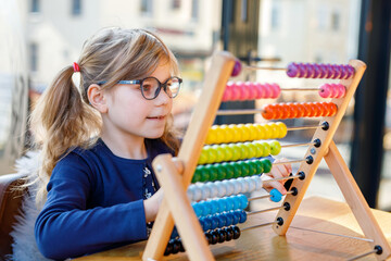 Little preschool girl playing with educational wooden rainbow toy counter abacus. Healthy happy child with glasses learning to count and colors, indoors on sunny day.