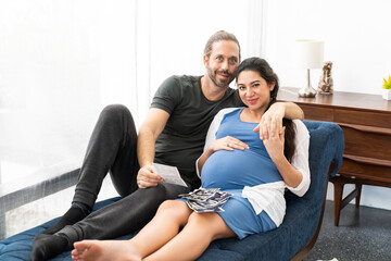 Obraz premium Hispanic male kiss and hug female couple. Beautiful pregnant woman and handsome husband smiling spend time togetherness at home.