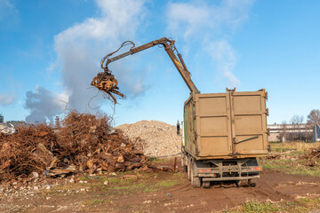 A grapple truck loads scrap industrial metal for recycling. Manipulator with a hydraulic magnetic crab against the sky. Crane garbage truck loading of industrial waste.