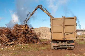 A grapple truck loads scrap industrial metal for recycling. Manipulator with a hydraulic magnetic crab against the sky. Crane garbage truck loading of industrial waste.