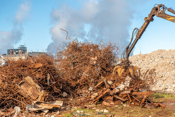 A grapple truck loads scrap industrial metal for recycling. Manipulator with a hydraulic magnetic crab against the sky. Crane garbage truck loading of industrial waste.