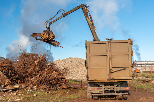 A grapple truck loads scrap industrial metal for recycling. Manipulator with a hydraulic magnetic crab against the sky. Crane garbage truck loading of industrial waste.