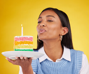 Birthday, cake and woman blowing candle in studio for happy party celebration on yellow background....