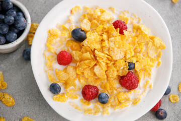 Tasty corn flakes with blueberries and raspberries in a black bowl, top view