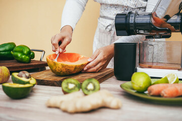 Young woman preparing organic juice with cold pressed extractor machine - Main focus on hands