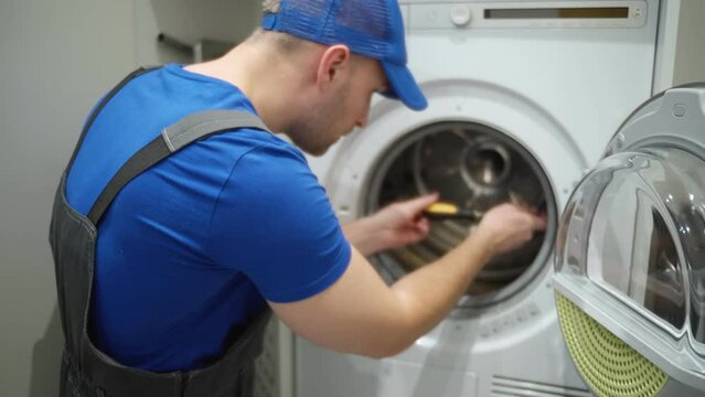 A young male technician repairing a washing machine in a laundry room at a client's home. 