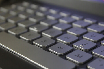 Closeup shot of a laptop gray keyboard with black colour font on black background, selective focus.