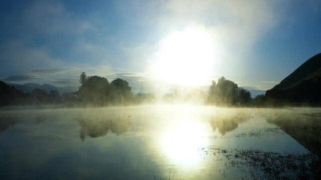 Steam from the warm lake water rising into the cold air with the sunrise reflecting off the water - time lapse