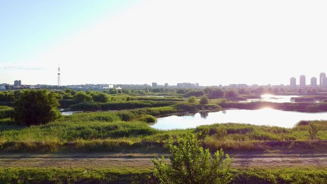 Side Motion Along A Dirt Sidewalk With The Beautiful Vacaresti Delta In The Background, Lush Green Vegetation, Small Lakes, Clear Blue Sky And Tall Buildings, Romania
