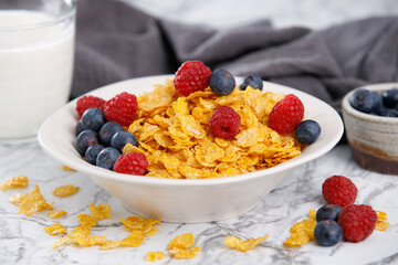 Tasty corn flakes with blueberries and raspberries in a black bowl with milk on marble table