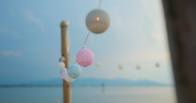 Illuminated soft pastel coloured ball string lights hanging glowing for paradise beachfront evening party