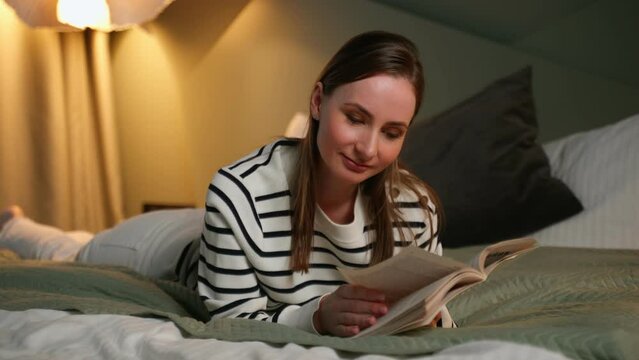 Leisure and people concept - young woman reading book in bed at night home. 