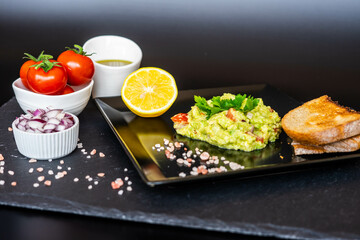 Homemade guacamole with red onion, cherry tomatoes, olive oil, pink salt and lemon juice, accompanied by toast . Home cooking, eating healthy, vegan food