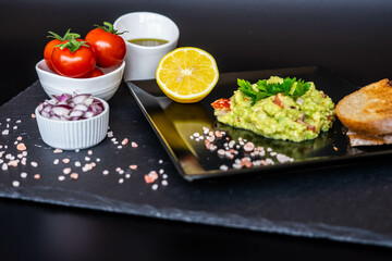 Homemade guacamole with red onion, cherry tomatoes, olive oil, pink salt and lemon juice, accompanied by toast . Home cooking, eating healthy, vegan food