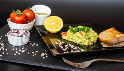 Homemade guacamole with red onion, cherry tomatoes, olive oil, pink salt and lemon juice, accompanied by toast . Home cooking, eating healthy, vegan food
