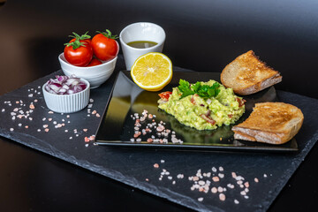 Homemade guacamole with red onion, cherry tomatoes, olive oil, pink salt and lemon juice, accompanied by toast . Home cooking, eating healthy, vegan food