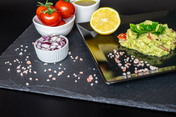 Homemade guacamole with red onion, cherry tomatoes, olive oil, pink salt and lemon juice, accompanied by toast . Home cooking, eating healthy, vegan food