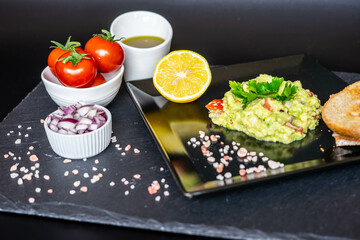 Homemade guacamole with red onion, cherry tomatoes, olive oil, pink salt and lemon juice, accompanied by toast . Home cooking, eating healthy, vegan food