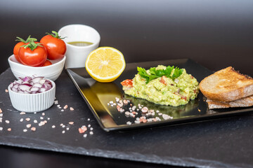 Homemade guacamole with red onion, cherry tomatoes, olive oil, pink salt and lemon juice, accompanied by toast . Home cooking, eating healthy, vegan food