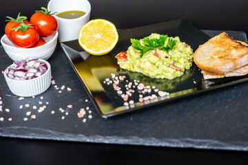 Homemade guacamole with red onion, cherry tomatoes, olive oil, pink salt and lemon juice, accompanied by toast . Home cooking, eating healthy, vegan food