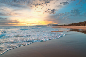 Mesmerizing sunset behind the clouds over pristine sandy beach on the Sunshine Coast in Australia. Wide angle beach panorama. 