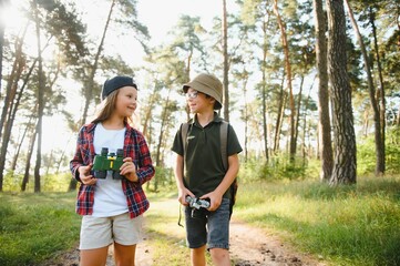 Happy excited school children with backpacks in casual clothes enjoying walk in forest on sunny autumn day, two active kids boy and girl running and playing together during camping trip in nature.