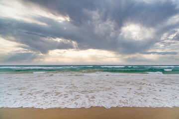 Beautiful wide panoramic view of the turquoise ocean waves crushing on the shore at dramatic sunrise on a stormy day.