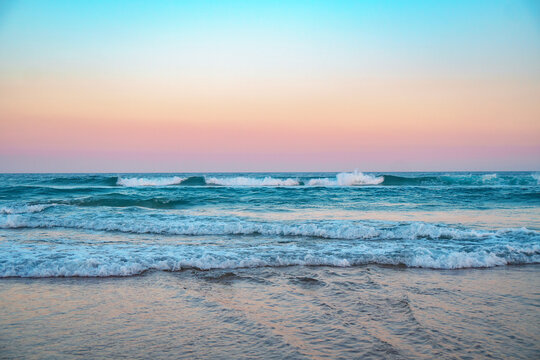 Spectacular panorama of the Pacific Ocean and crushing surfing waves against the pristine beach during beautiful sunrise.