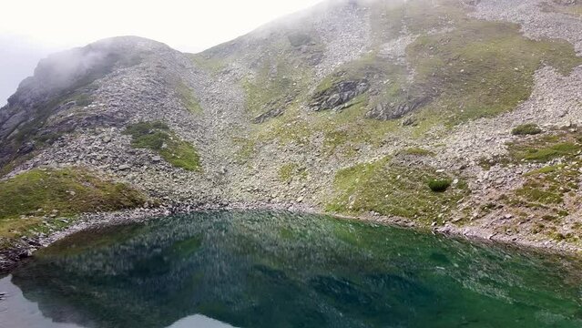 Aerial Slow Motion Over A Mountain Lake With Crystal Clear Water, Surrounded By Small Limestone White Rocks With Clouds Slowly Forming Around The Scene, Iezer Lake, Transylvania, Romania, Europe