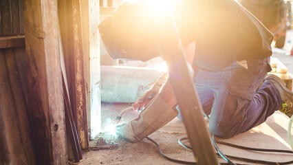 backlit worker welding an iron on the ground
