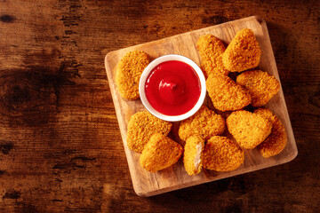Chicken nuggets with ketchup on a rustic wooden table, shot from the top with a place for text. Crispy snack