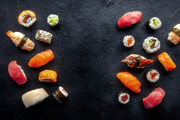 Obraz na płótnie Canvas Sushi frame, a flat lay, top shot. Rolls, maki, nigiri on a black slate background, Japanese food. Salmon, eel, shrimp, tuna etc with rice, with a place for text