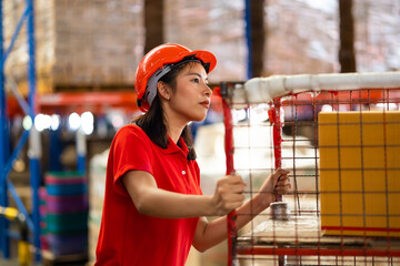 Warehouse female staff worker wearing hardhat helmet standing by goods shelf working pulling a pallet truck in large warehouse factory. Asian engineer woman © NVB Stocker
