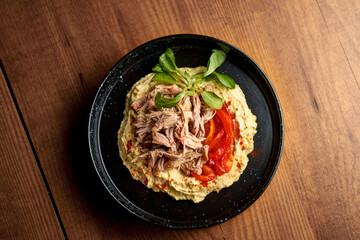 Hummus with chicken and pita in a black plate. Wooden background