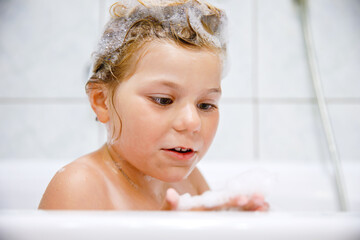 Cute child with shampoo foam and bubbles on hair taking bath. Portrait of happy smiling preschool girl health care and hygiene concept. Washes hair by herself.