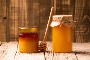 Honey in glass closed jars and a wooden dipper on a wooden background.