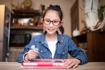 自宅でタブレット学習をするメガネをかけた女の子