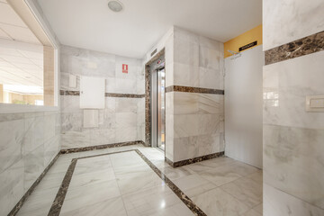 Interior portal of a residential building with white marble floors and marble tiles next to the elevator