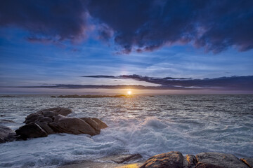 Sunset over some reefs beaten by the waves on the Galician coast of Spain with heavy clouds of water