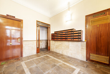 Portal of a simple residential building with mailboxes and varnished sapele doors