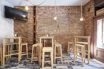 An empty bar with raw brick walls and tall white wooden tables with matching stools, a wooden mosaic floor and a television