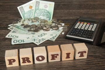 banknoty, bilon wraz z kalkulatorem na stole. Klocki drewniane z napisem PROFIT © siwyk