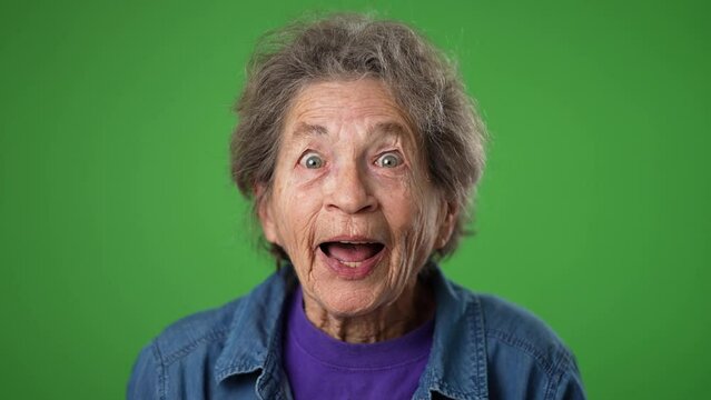 Closeup slow motion portrait of excited smiling elderly senior old woman winner with wrinkled skin and grey hair on green screen background.